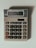 A beige calculator with multiple buttons, featuring a display that shows the number 3.14. The calculator has a solar panel and various function keys, including numerical digits, mathematical operations, and memory functions.