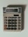 A beige calculator with multiple buttons, featuring a display that shows the number 3.14. The calculator has a solar panel and various function keys, including numerical digits, mathematical operations, and memory functions.