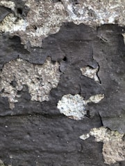 Peeling paint and rough texture of an old wall with uneven surface and patches of darker and lighter shades.