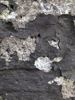Peeling paint and rough texture of an old wall with uneven surface and patches of darker and lighter shades.