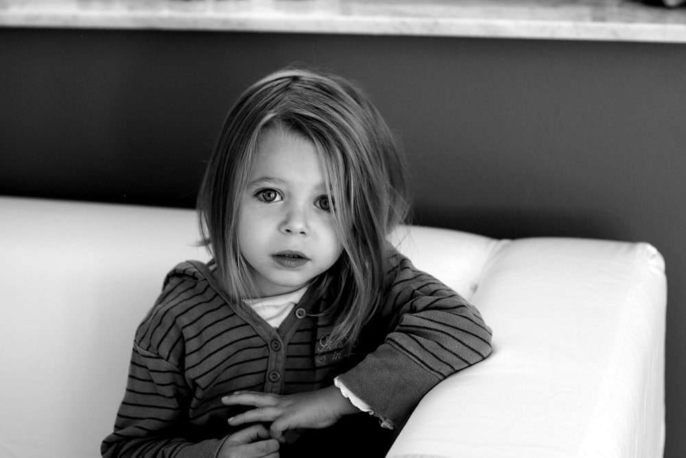 a little girl sitting on top of a white couch