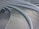 Curved metal grates arranged in a series of parallel, concentric arcs. The surface is sleek and modern, with shadows casting lines across the walkway from a railing. The design is likely part of an architectural structure, showcasing a clean and contemporary aesthetic.
