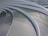 Curved metal grates arranged in a series of parallel, concentric arcs. The surface is sleek and modern, with shadows casting lines across the walkway from a railing. The design is likely part of an architectural structure, showcasing a clean and contemporary aesthetic.