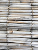 A tightly packed arrangement of aged, horizontally stacked bamboo poles with visible weathering and slight discoloration.