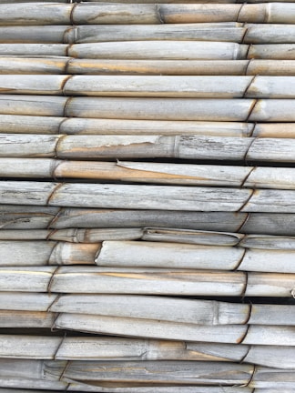 A tightly packed arrangement of aged, horizontally stacked bamboo poles with visible weathering and slight discoloration.