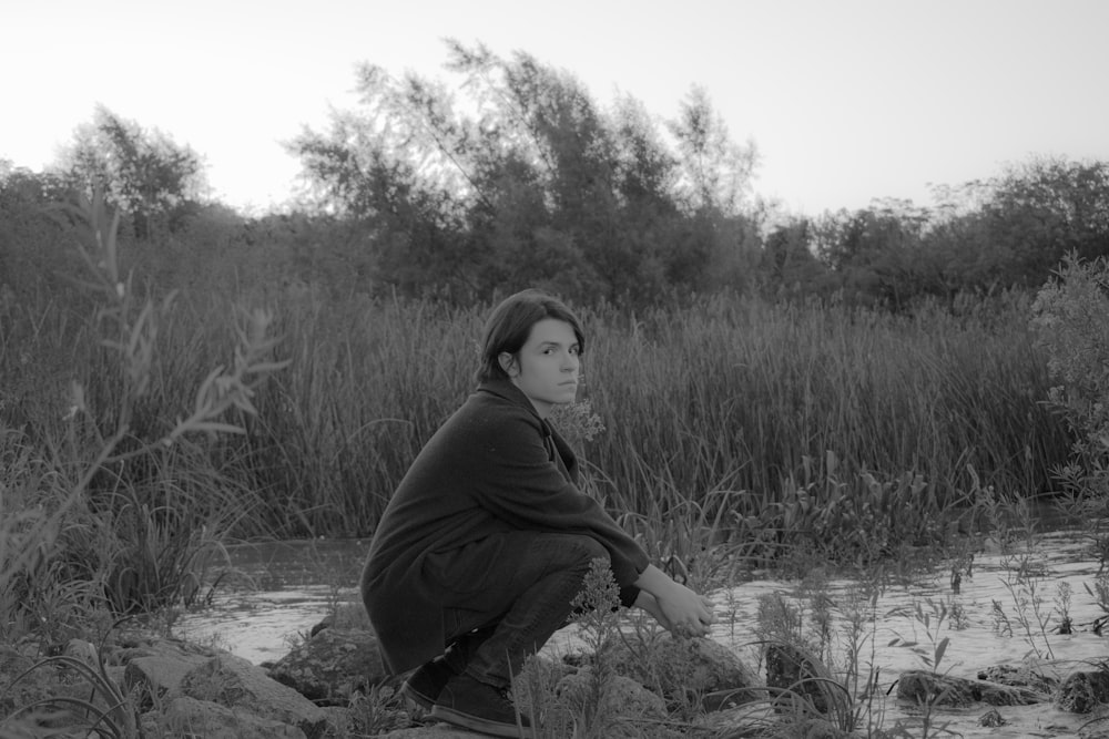 a woman sitting on top of a rock next to a river