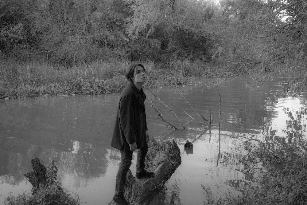 a black and white photo of a woman standing on a log