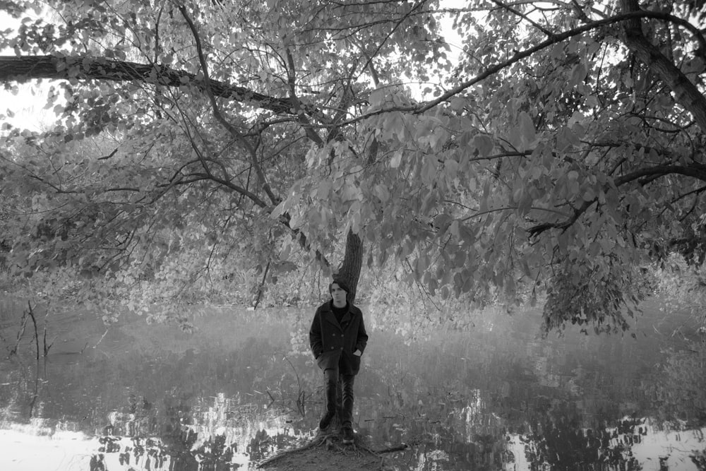 Una foto in bianco e nero di una persona in piedi accanto a un albero