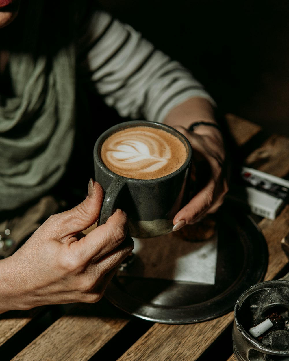 a woman holding a cup of coffee on top of a wooden table