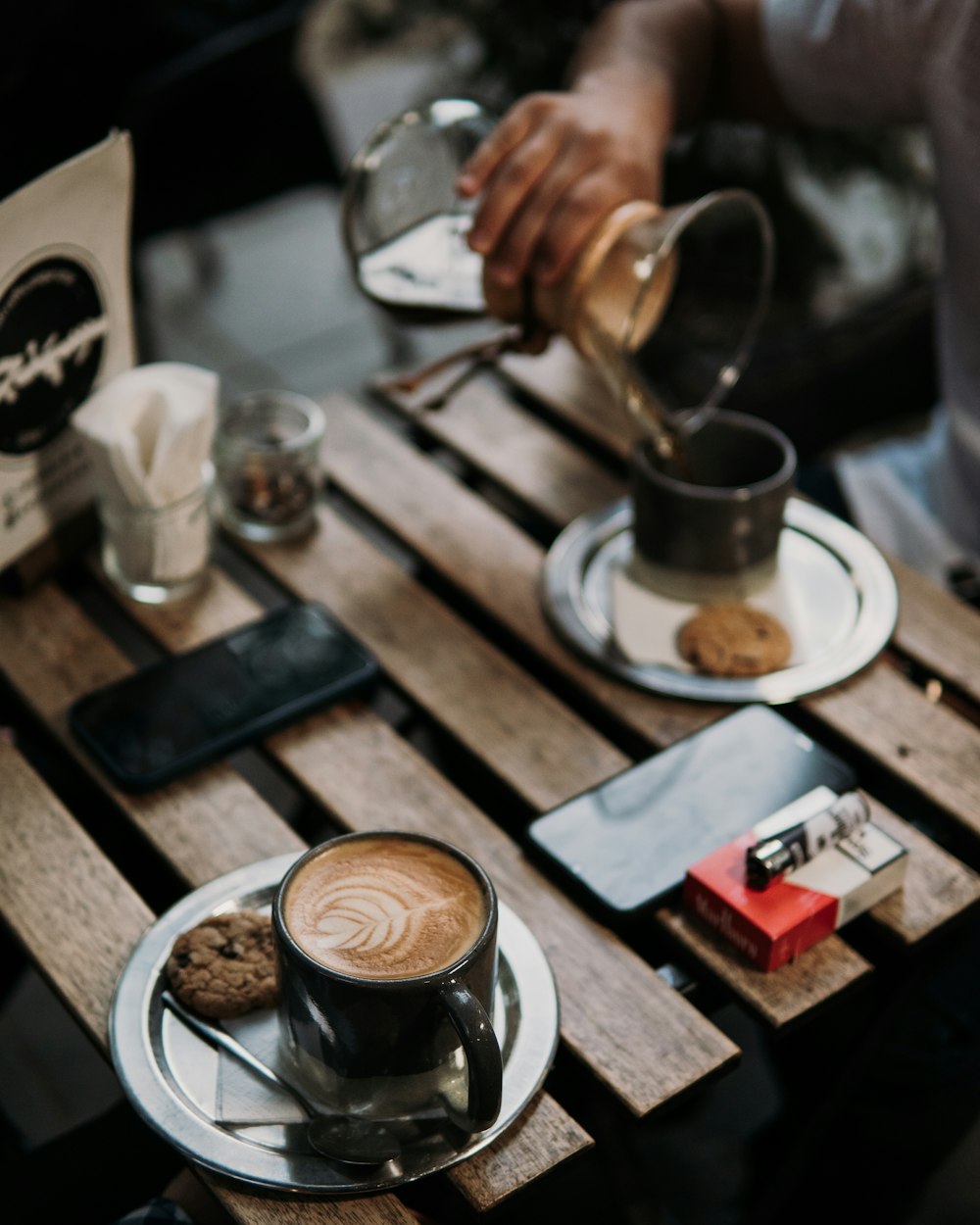 a person pouring a cup of coffee on top of a wooden table