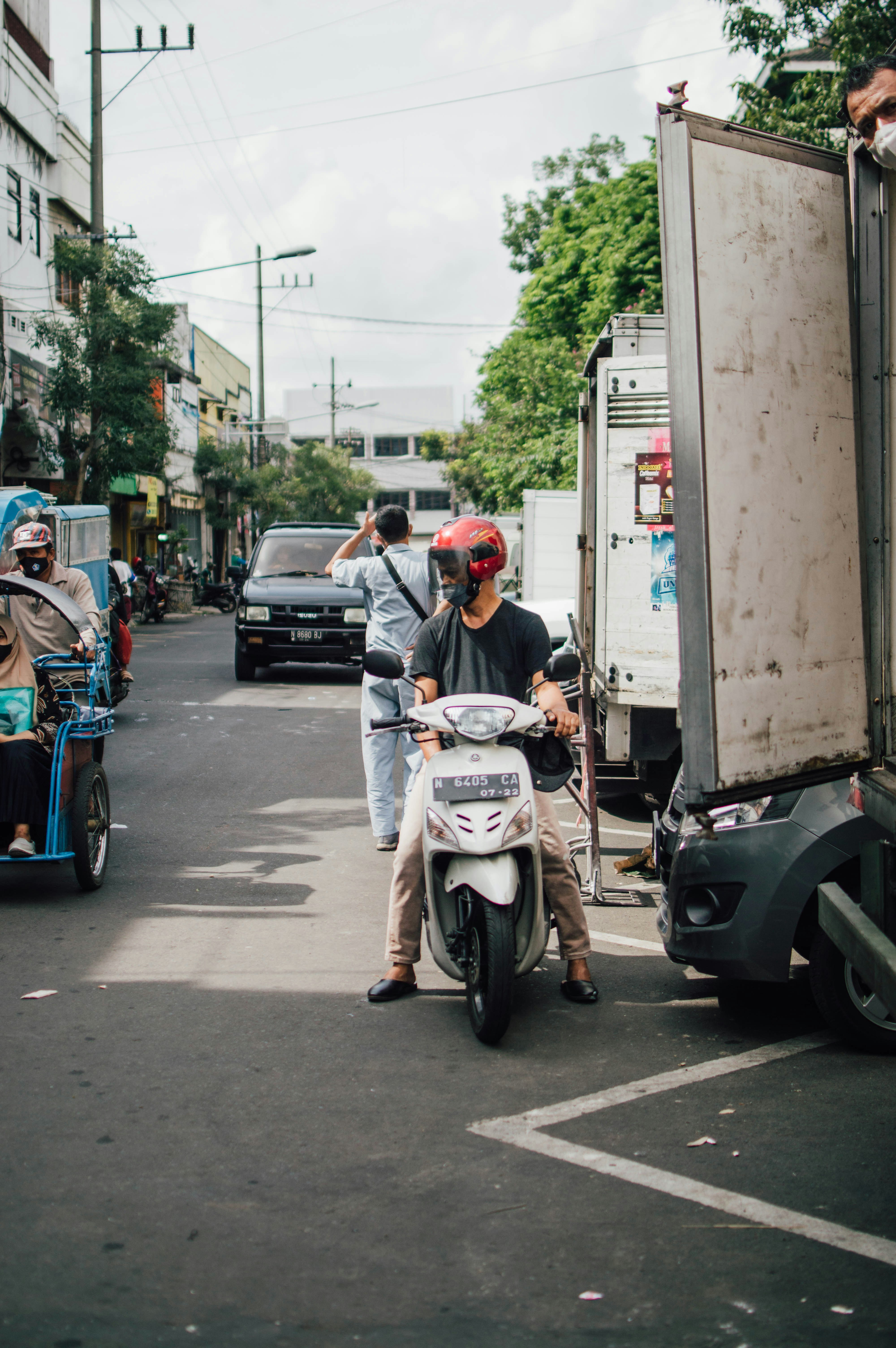 Seorang pria mengendarai sepeda motor di jalan di sebelah truk