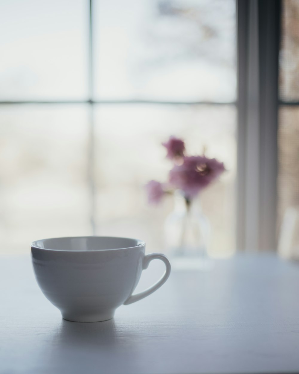 una tazza bianca seduta sopra un tavolo accanto a un vaso di fiori