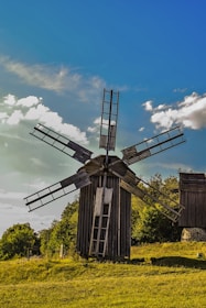 Windmills turning gently on a lush green hill beside a modern hospital.