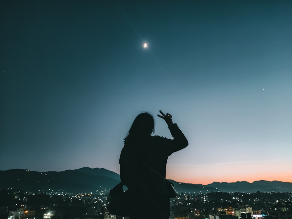 a woman standing on top of a hill looking at the sky