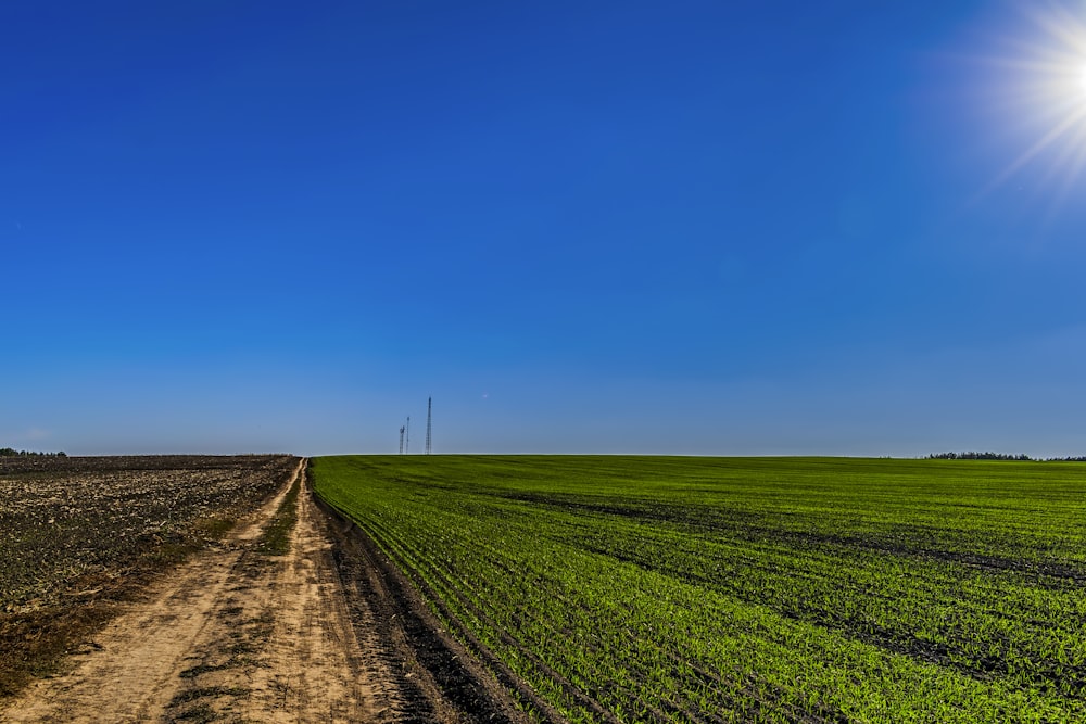 a dirt road running through a green field under a blue sky