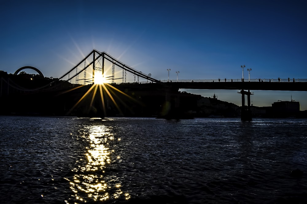 the sun is setting over a bridge over a body of water