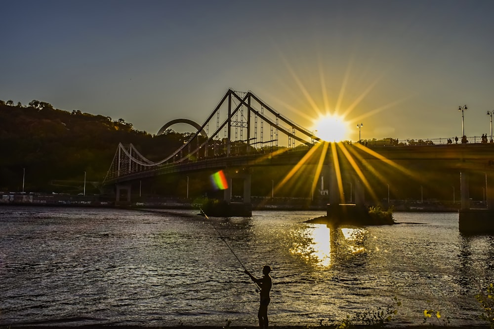 the sun is setting over a bridge over a body of water