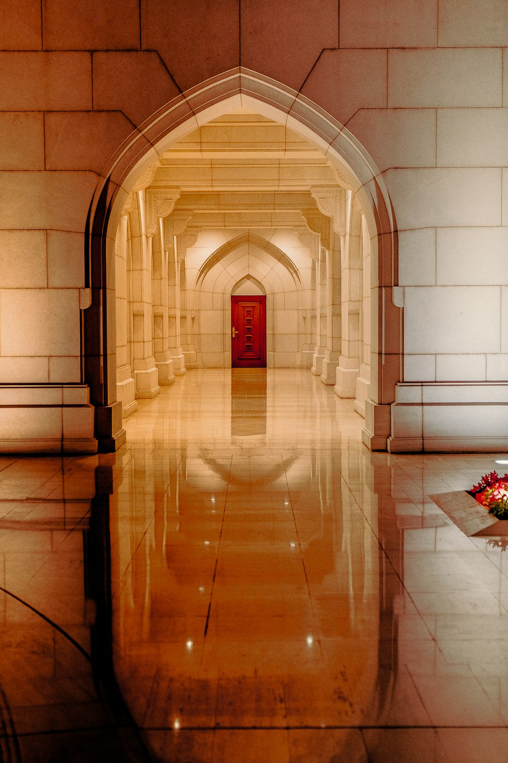 un long couloir avec une porte rouge et des fleurs sur le sol