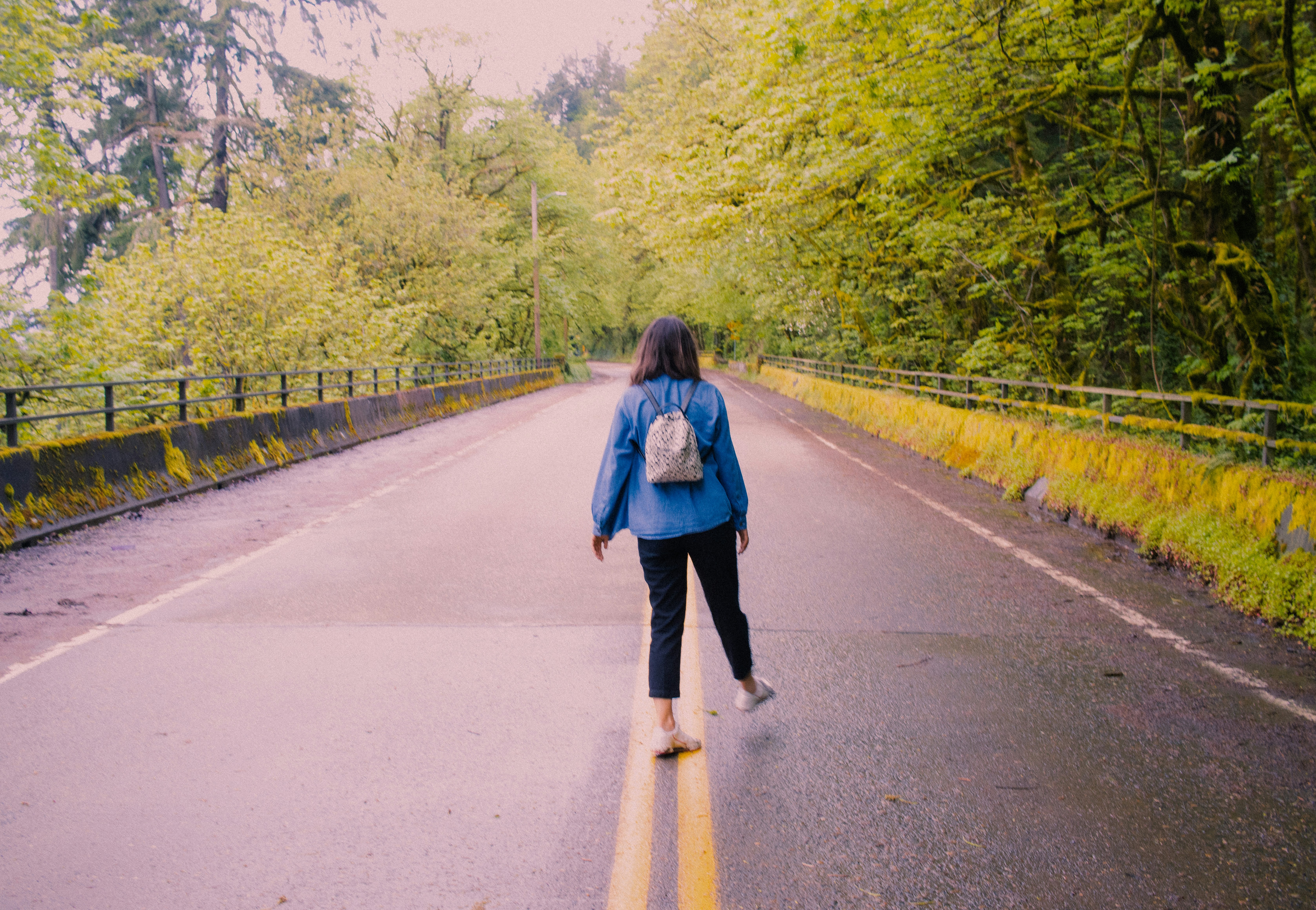 a woman walking down a road in the middle of a forest