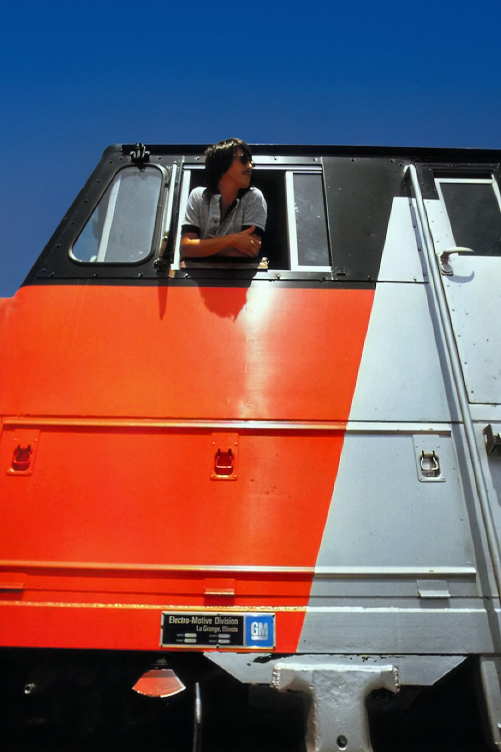 a man sitting in the window of an orange and silver train