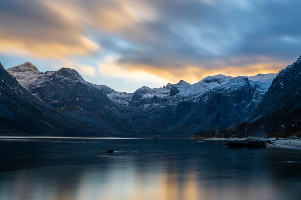 a lake surrounded by mountains under a cloudy sky