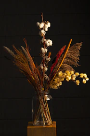 An arrangement of dried flowers in a weathered metal vase on a reclaimed wood table.