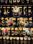 A display of bamboo lanterns with intricate patterns carved into their surfaces, illuminated from within. The lanterns are arranged in rows and accompanied by colorful artificial flowers interspersed among them.