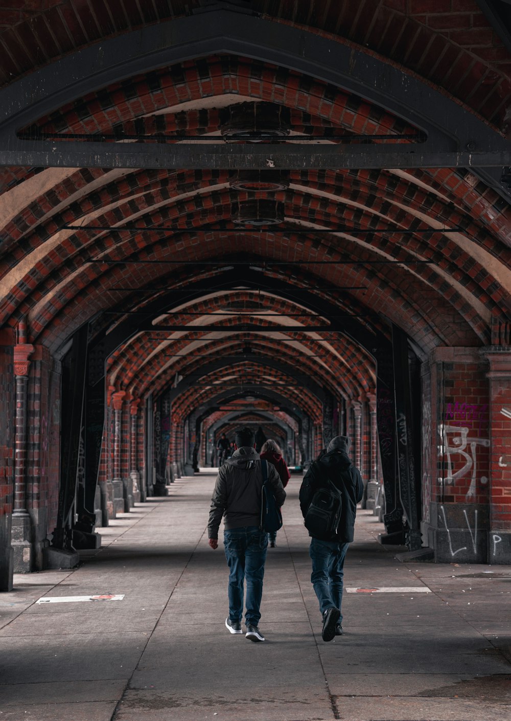 a couple of people walking down a street under a bridge