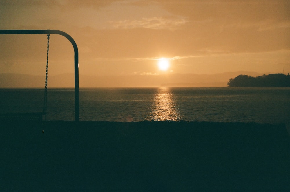 a sunset over a body of water with a swing in the foreground