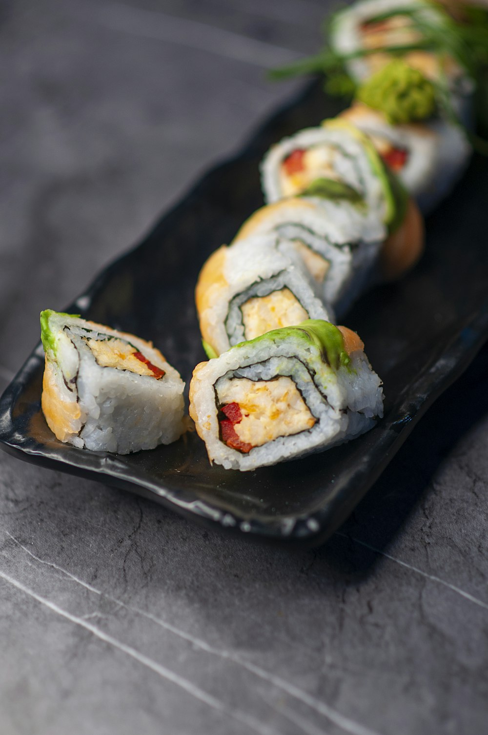 a black plate topped with sushi rolls on top of a table