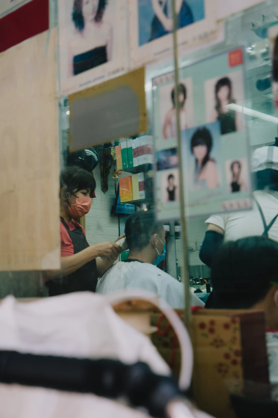 Two hairdressers work on clients' hair in a well-lit salon with framed artwork nearby