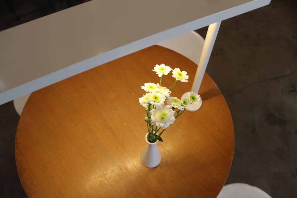 a white vase filled with white flowers on top of a wooden table