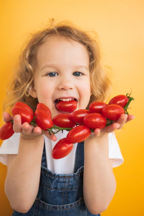 a little girl holding up a bunch of tomatoes