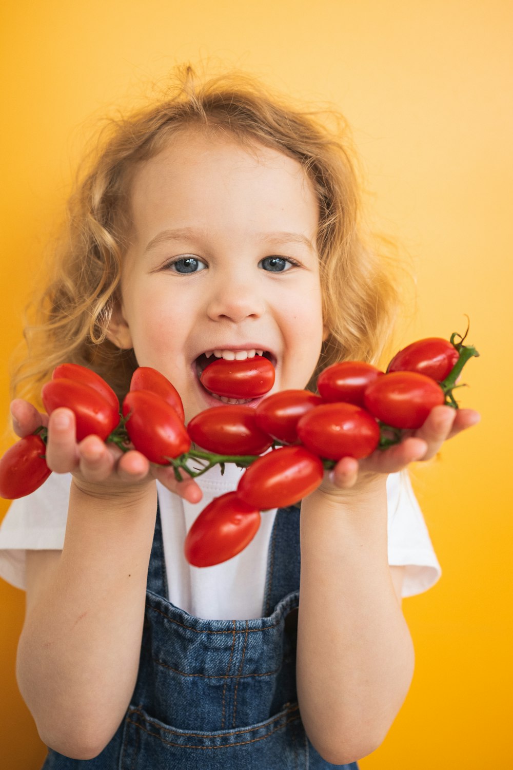 a little girl holding up a bunch of tomatoes