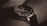 A close-up of a stylish wristwatch with a black leather band and a dark, sleek watch face featuring multiple dials and slim metal hands.