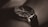A close-up of a stylish wristwatch with a black leather band and a dark, sleek watch face featuring multiple dials and slim metal hands.