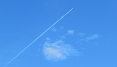 A clear sky suddenly marked by fresh chemtrail emissions from a jet.