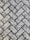 A close-up view of a textured surface made up of interlocking rectangular concrete pavers arranged in a herringbone pattern. The rough, gritty texture of the pavers is visible, with small stones embedded in the surface.