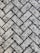 A close-up view of a textured surface made up of interlocking rectangular concrete pavers arranged in a herringbone pattern. The rough, gritty texture of the pavers is visible, with small stones embedded in the surface.