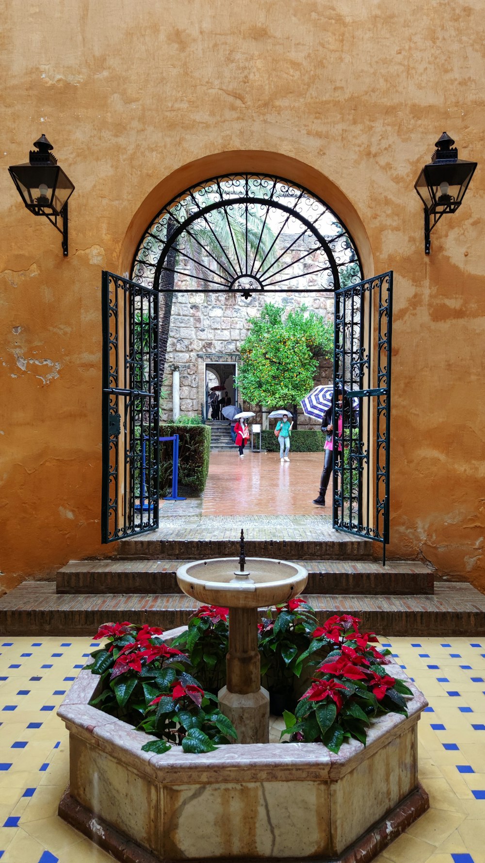 a courtyard with a fountain and a couple of people with umbrellas