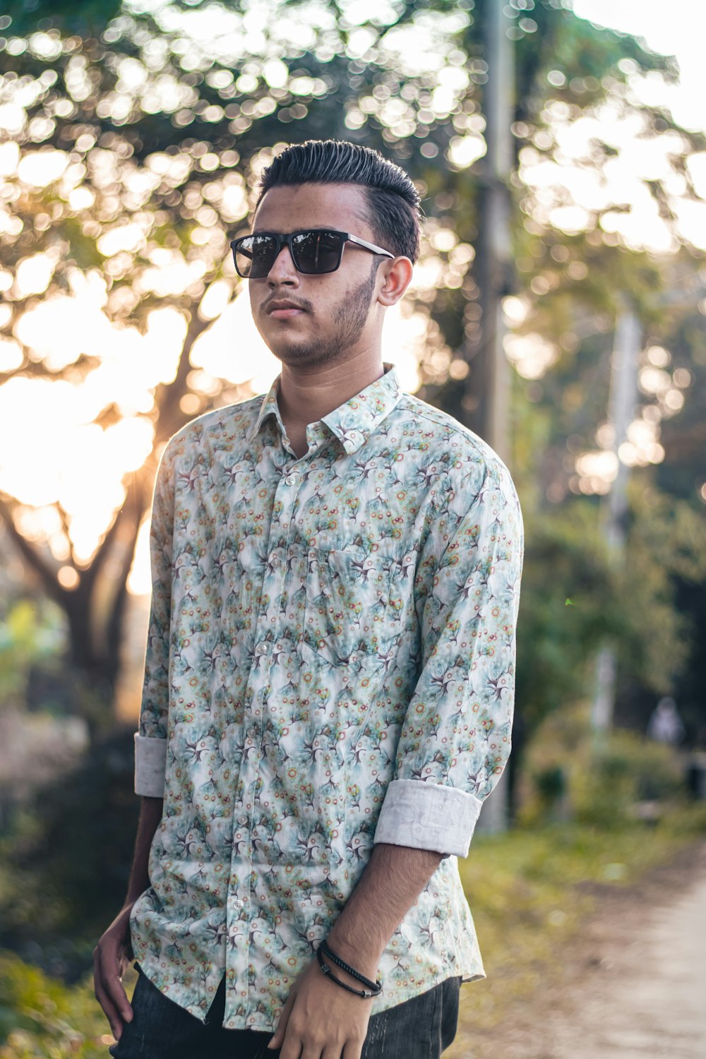 a man wearing sunglasses standing on a dirt road