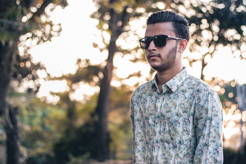 a man wearing sunglasses standing in front of trees