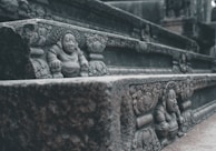 A detailed stone carving of a historical or mythological figure is intricately designed on the side of an ancient structure. The carving features ornate patterns and an expressive face, set within a series of weathered steps.