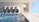 A clean, tiled indoor pool area with four large, cylindrical pipes on the wall. The pool water reflects light, creating dynamic patterns. A ramp with handrails leads down into the water, and there's a bright, rectangular passageway leading outside.