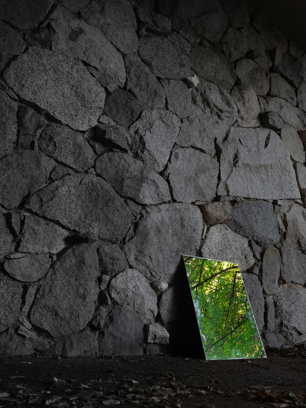 a mirror sitting on the ground in front of a stone wall