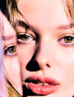 A close-up and artistic portrait features a woman's face with a mirrored effect, highlighting her green eyes, skin texture, and glossy lips. The image captures details of her eyebrows, lashes, and natural complexion, creating an intriguing visual effect.