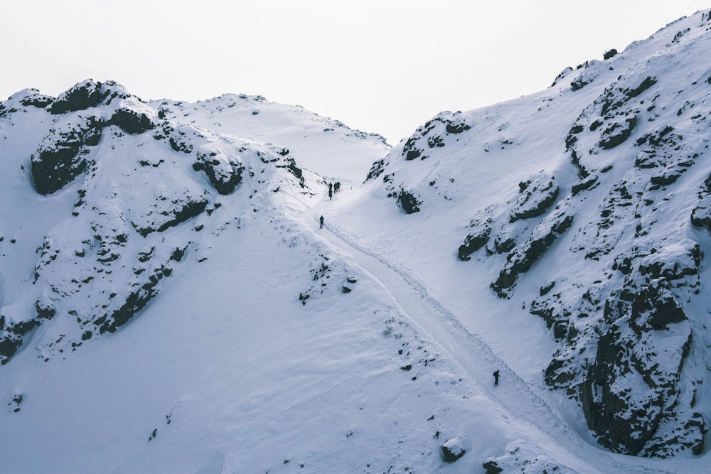 a couple of people walking up the side of a snow covered mountain