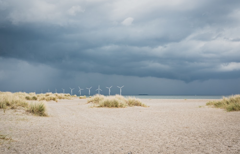 a group of wind mills on a beach under a cloudy sky