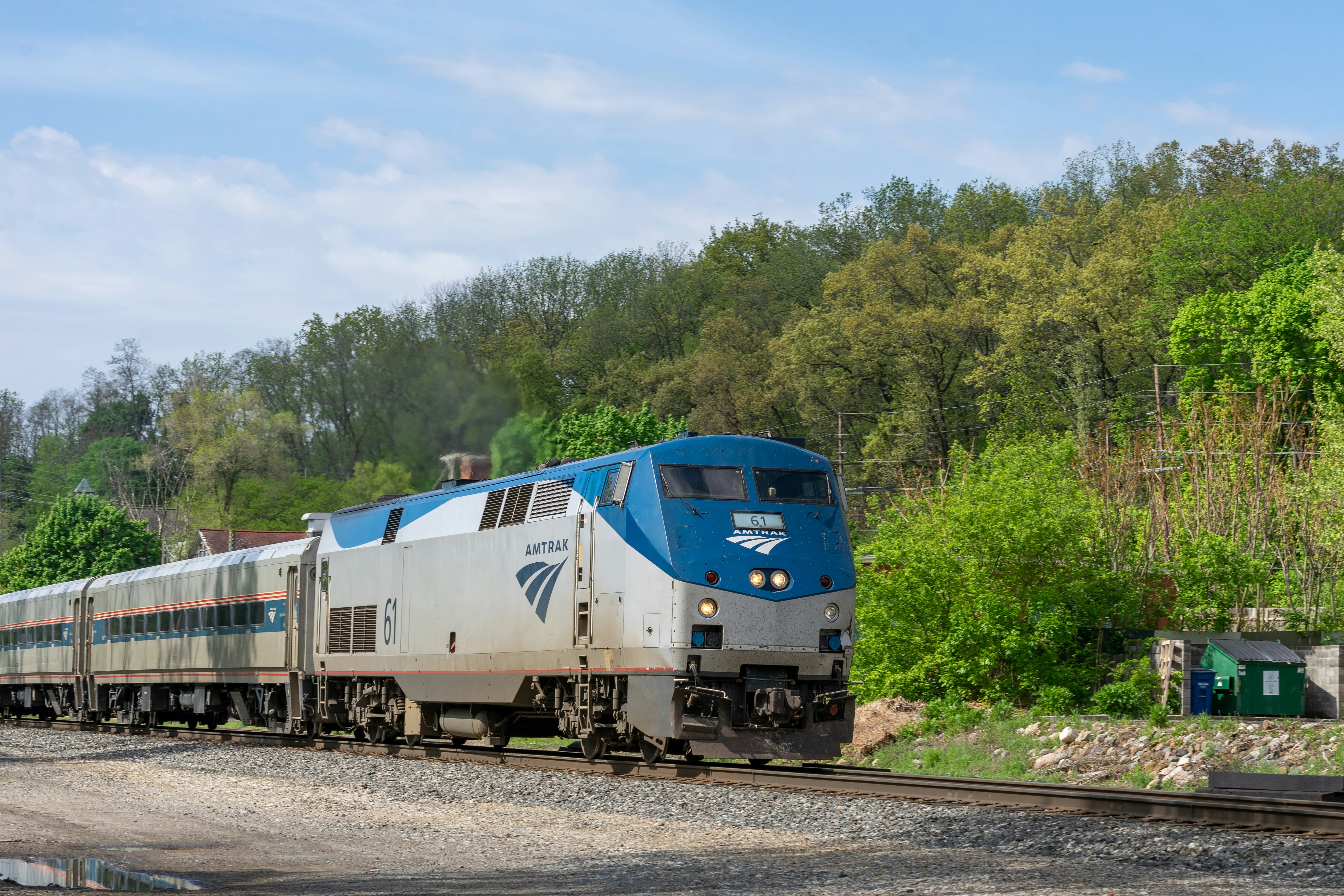 a blue and white train traveling down train tracks, An Amtrak train picking up speed out of Ann Arbor on a beautiful spring morning.