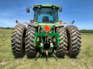 A sturdy tractor parked in a lush green field under a clear blue sky.